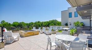 Une terrasse extérieure avec des chaises et des tables blanches, un foyer et une vue sur un immeuble moderne doté d’un balcon.