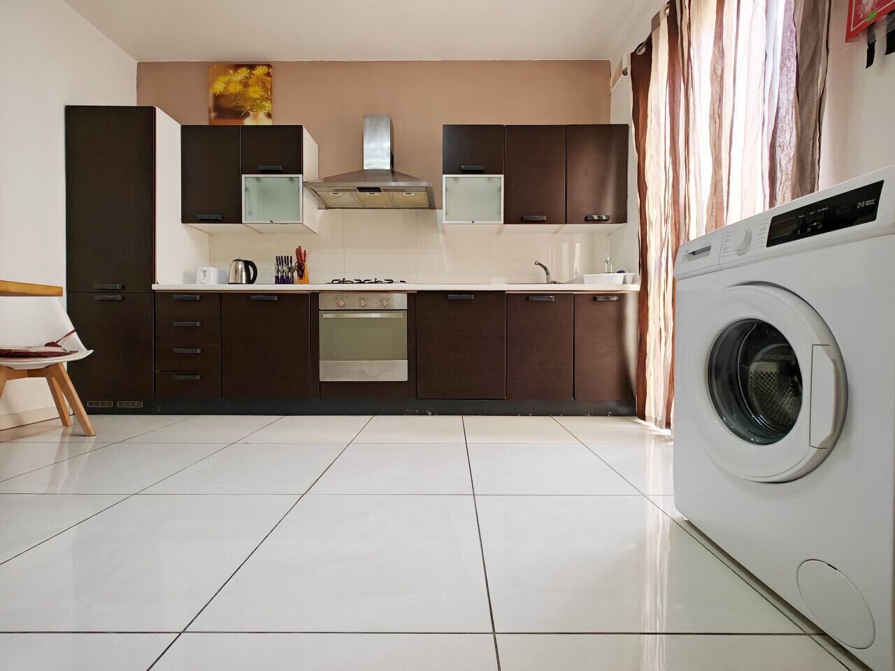 Une cuisine moderne avec des meubles de couleur sombre, une hotte de cuisine en acier inoxydable, un four encastré, un lave-vaisselle et un lave-linge à chargement frontal.
