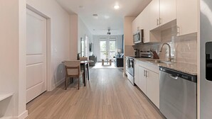 A modern kitchen with stainless steel appliances, a dining area with a table and chairs, and a view of the living room through an open door. - Landing | Stylish 1BD, Pool, Gym (Austin)