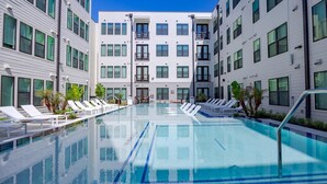 A modern hotel with a central swimming pool surrounded by lounge chairs and palm trees. - Landing | Beautiful 1BD, Gym, Pool (Austin)