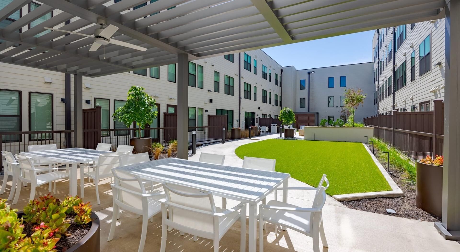 An outdoor patio area with white tables and chairs, a small lawn, and a building in the background.