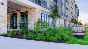 A modern building with a stone facade, large windows, and a sign indicating 'SOFI AT 6311 LEASING'. - Landing | Beautiful 1BD, Gym, Pool (Austin)