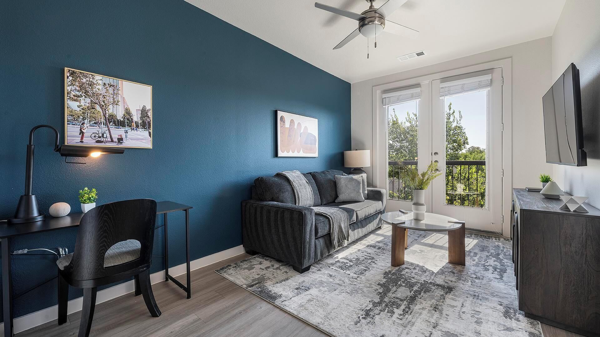 En moderne stue med en mørkeblå accentvæg, en sofa, et sofabord, et skrivebord med lampe og et fjernsyn.