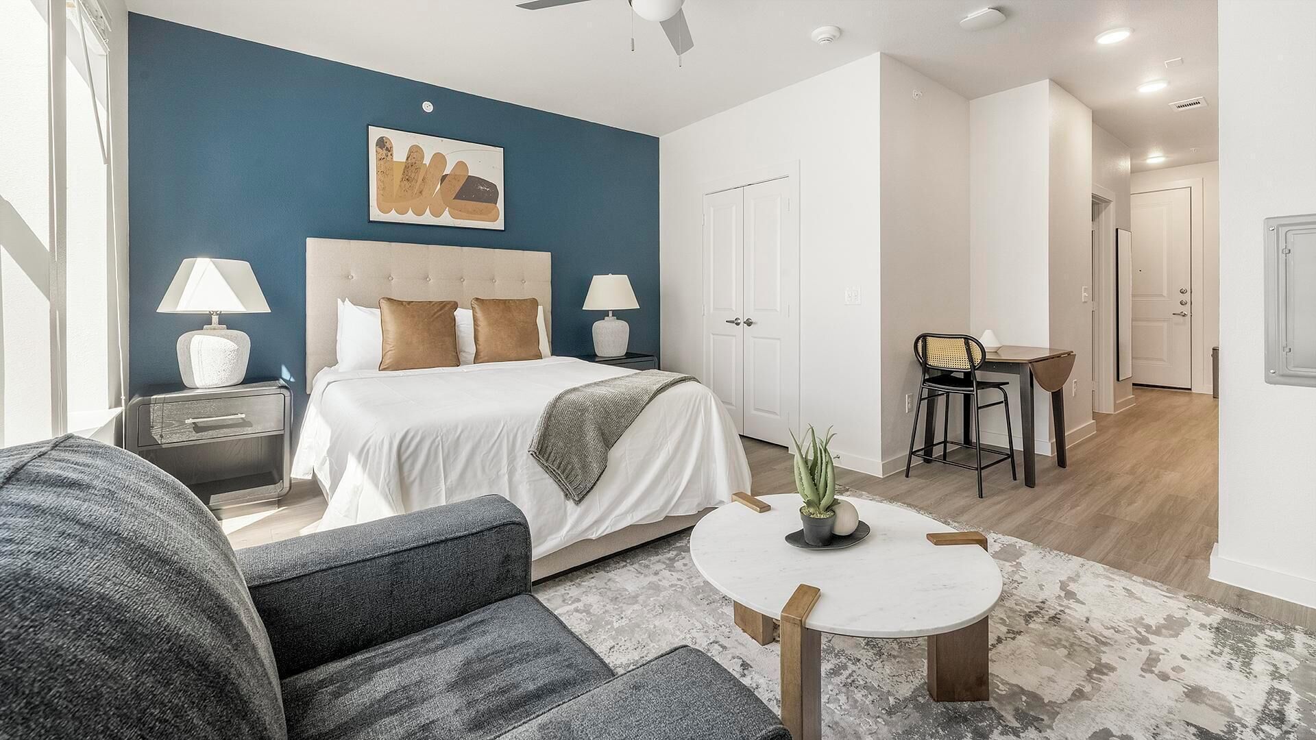 A modern hotel room with a large bed, a small round table, a sofa, and a dining area.
