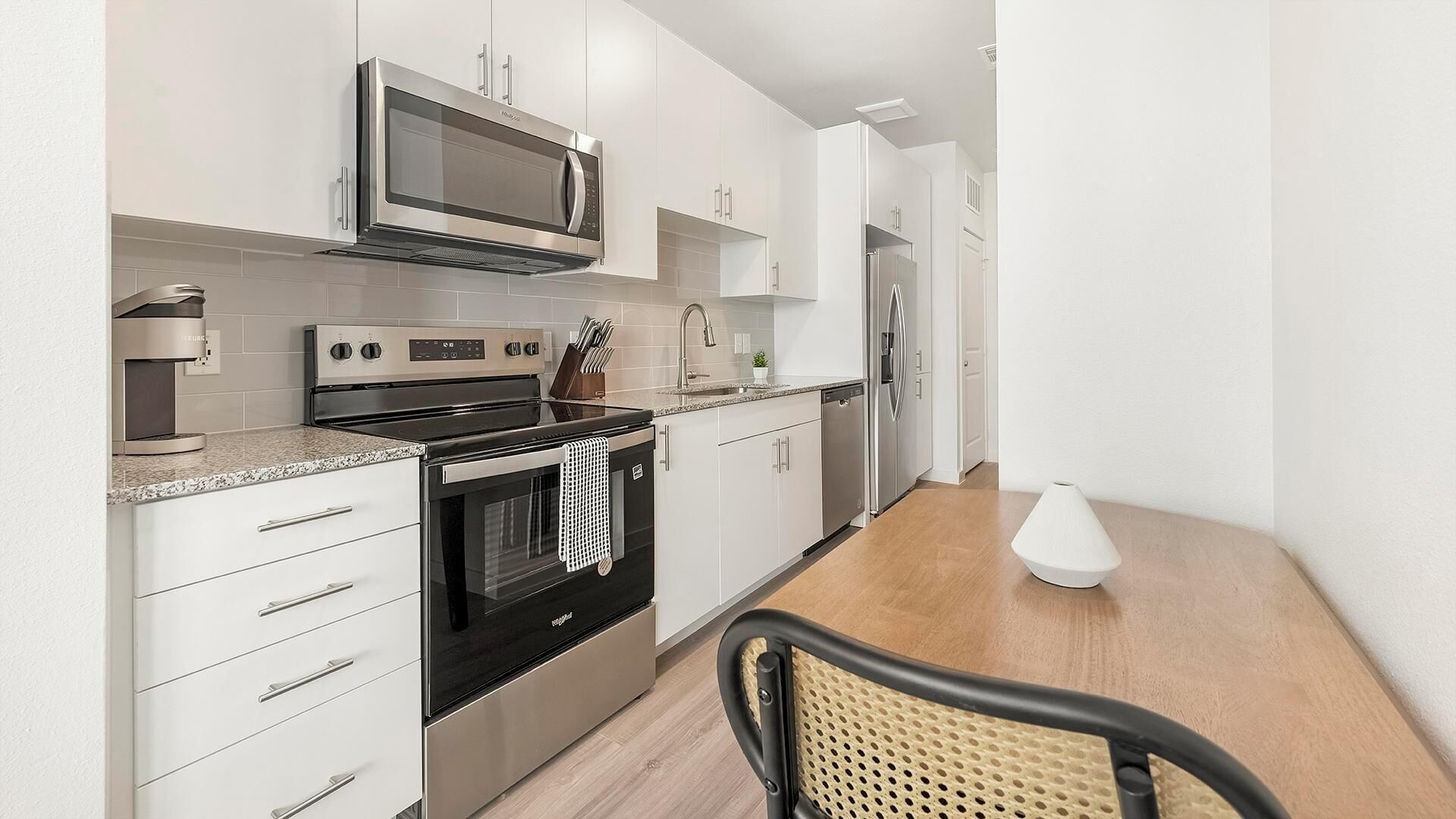 A modern kitchen with stainless steel appliances, white cabinetry, and a wooden dining table.