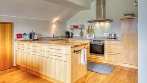 Eine moderne Küche mit Holzausstattung, einer großen Kochinsel, Edelstahlgeräten und einem eingebauten Ofen.