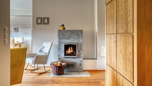 Ein Wohnzimmer mit Kamin aus Stein, einem Schaukelstuhl, einem Holzschrank und einem Holzkorb mit Brennholz.