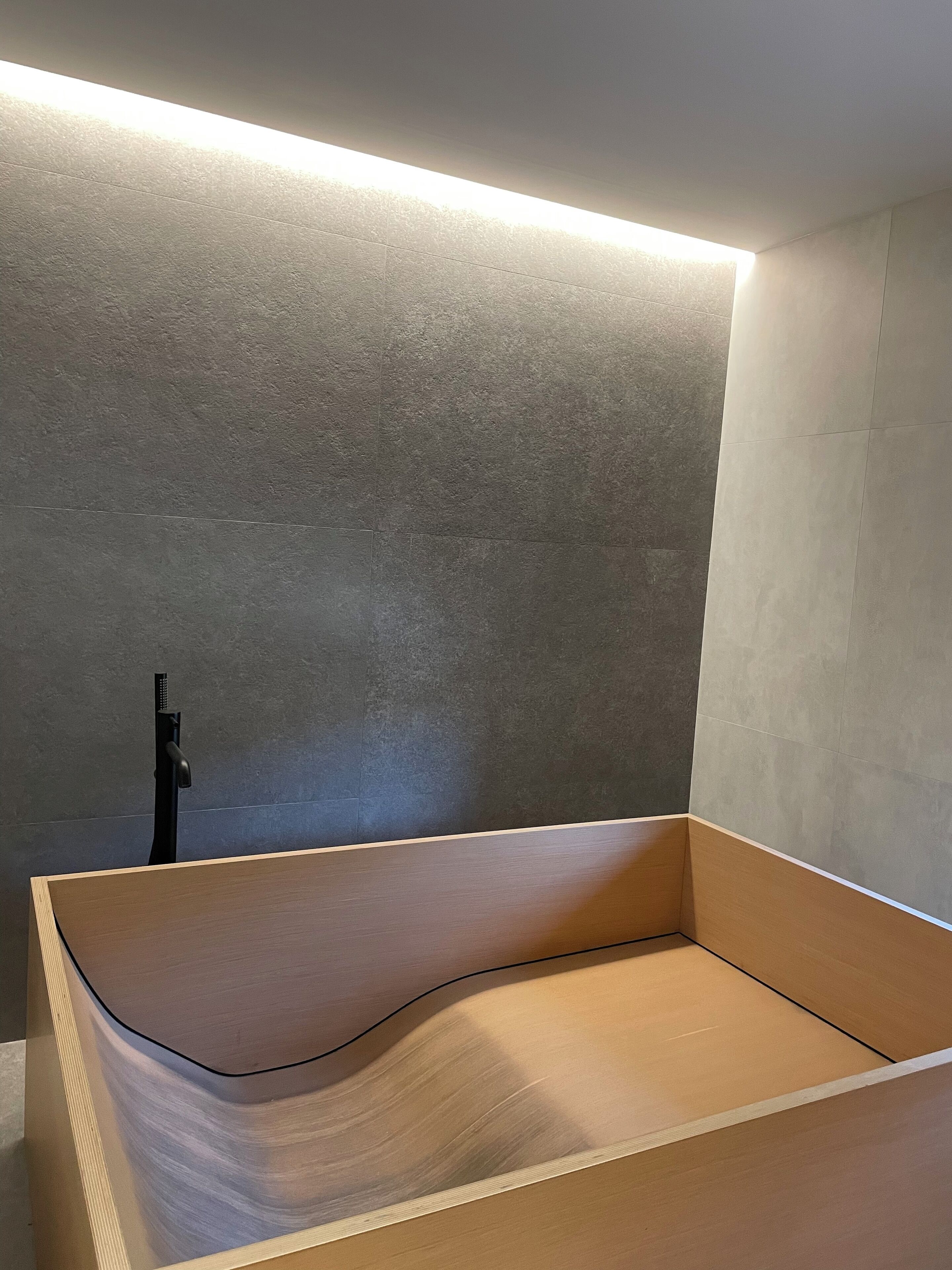 A modern bathroom with a wooden bathtub, a wall-mounted faucet, and a ceiling light.