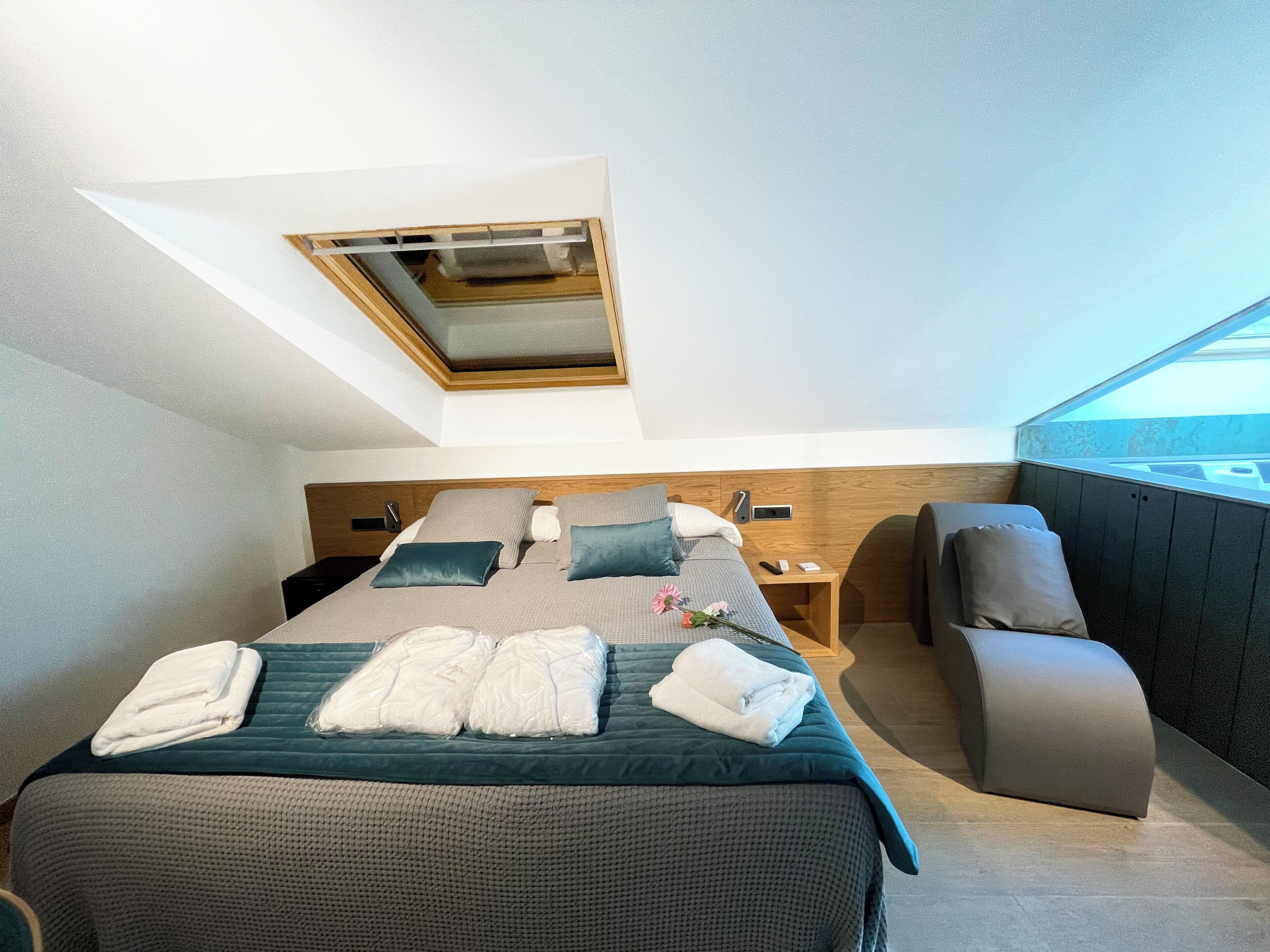 A modern hotel room with a large bed, a desk, a chair, and a skylight.