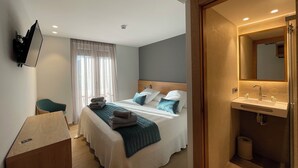 Une chambre d’hôtel équipée d’un lit, d’un bureau, d’une télévision et d’une salle de bain avec un miroir et un lavabo.