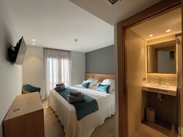 Una habitación de hotel con cama, escritorio, televisor y baño con espejo y lavamanos.