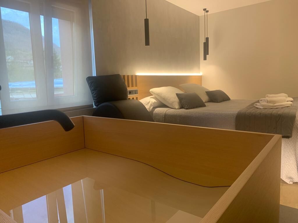 Een moderne slaapkamer met een houten hoofdbord, een bed met grijze beddengoed en een nachtkastje.