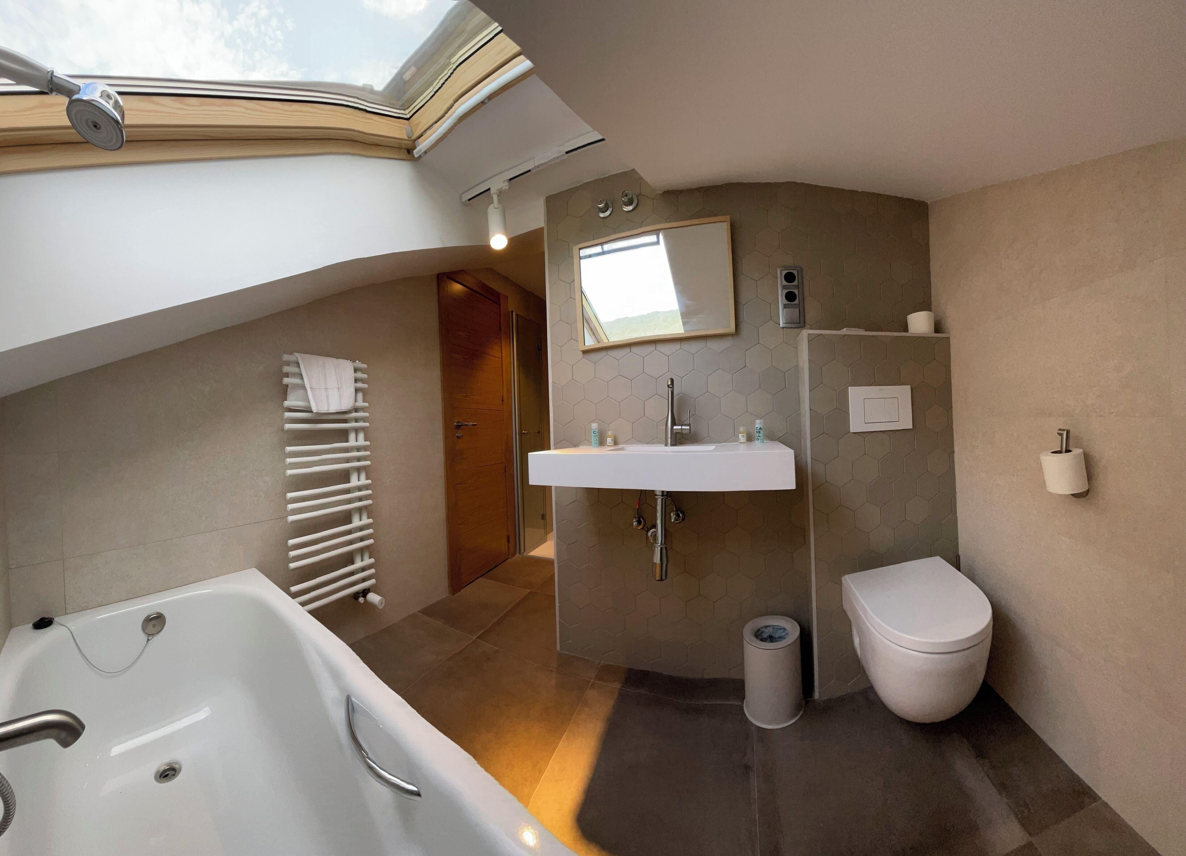 A modern bathroom with a skylight, a bathtub, a sink, and a toilet.