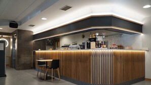 Un espace d’accueil moderne comprenant un comptoir de réception en bois, une machine à café et un coin salon avec des fauteuils.