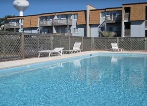 A swimming pool with lounge chairs, a water tower, and a building with balconies. - Anchor & Dreams - Peaceful Updated 2BR Oceanfront Condo (Ocean Isle Beach)