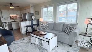 A modern kitchen with white cabinets, a refrigerator, and a dining area with two chairs. - Anchor & Dreams - Peaceful Updated 2BR Oceanfront Condo (Ocean Isle Beach)