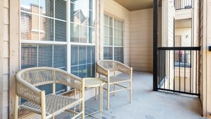 Un balcon avec deux fauteuils en osier et une petite table ronde, donnant sur un quartier résidentiel.