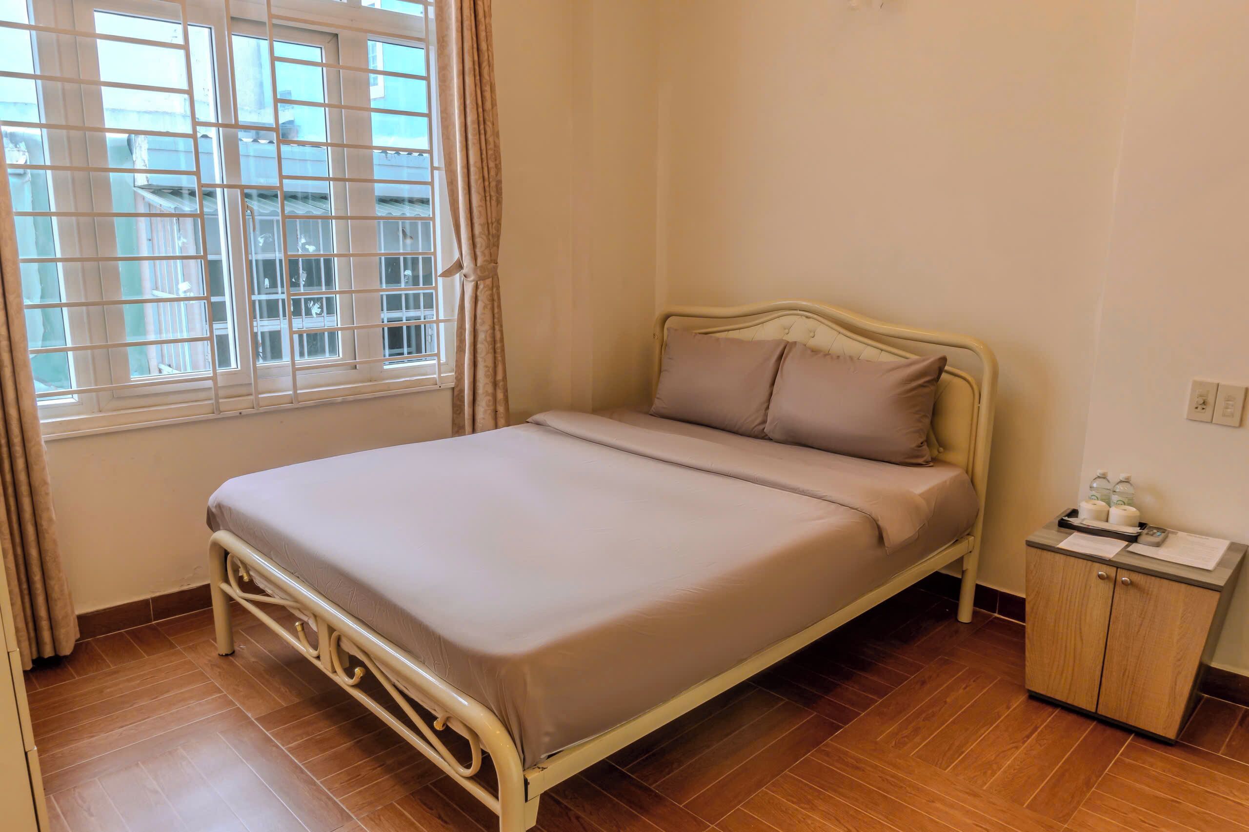 A neatly made bed with a headboard, a bedside table with a lamp, and a window with curtains.