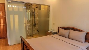 Ein Schlafzimmer mit einem hölzernen Bett, einem Nachttisch, einem kleinen Tisch und einer separaten Duschkabine aus Glas.