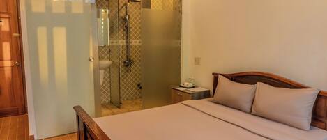 A bedroom with a wooden bed, a nightstand, a small table, and a glass-enclosed shower area.