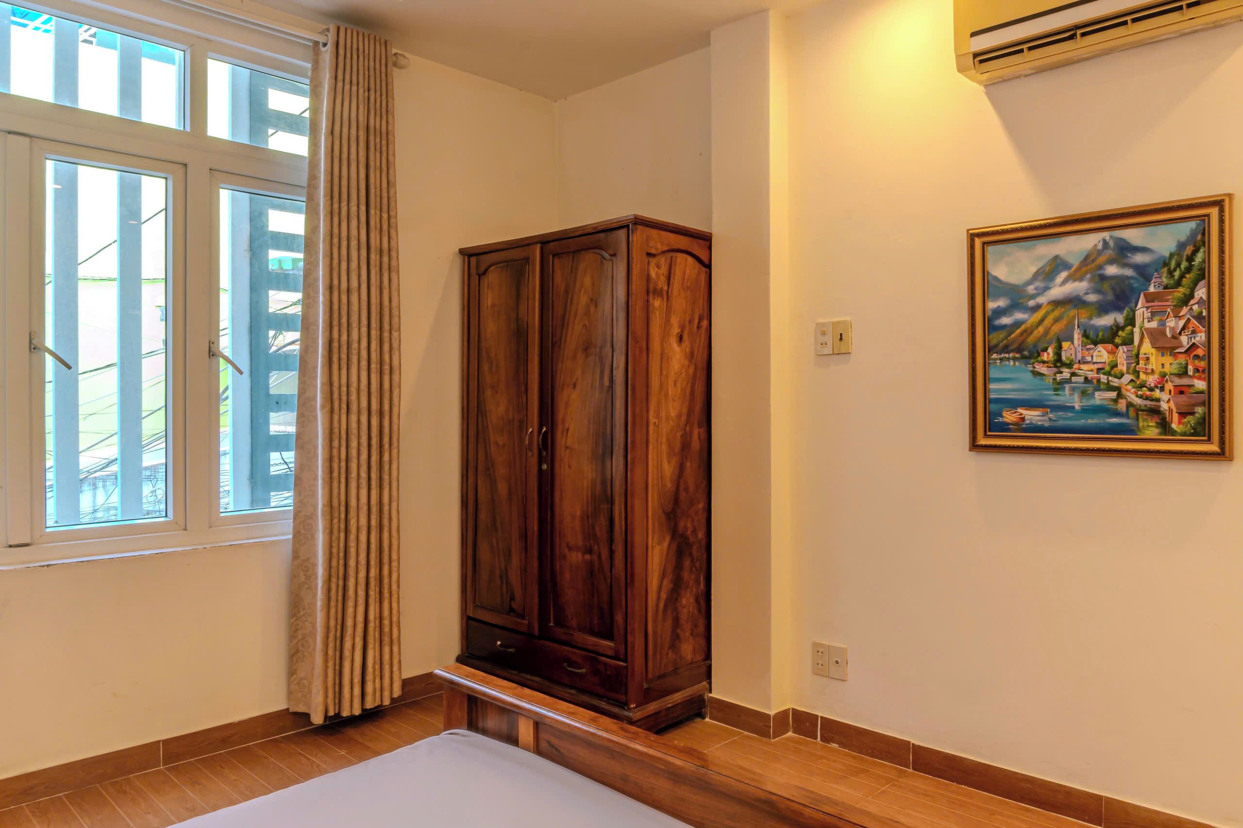 Ein Zimmer mit großem Holzschrank, einem Bild an der Wand und einem Fenster mit Vorhängen.