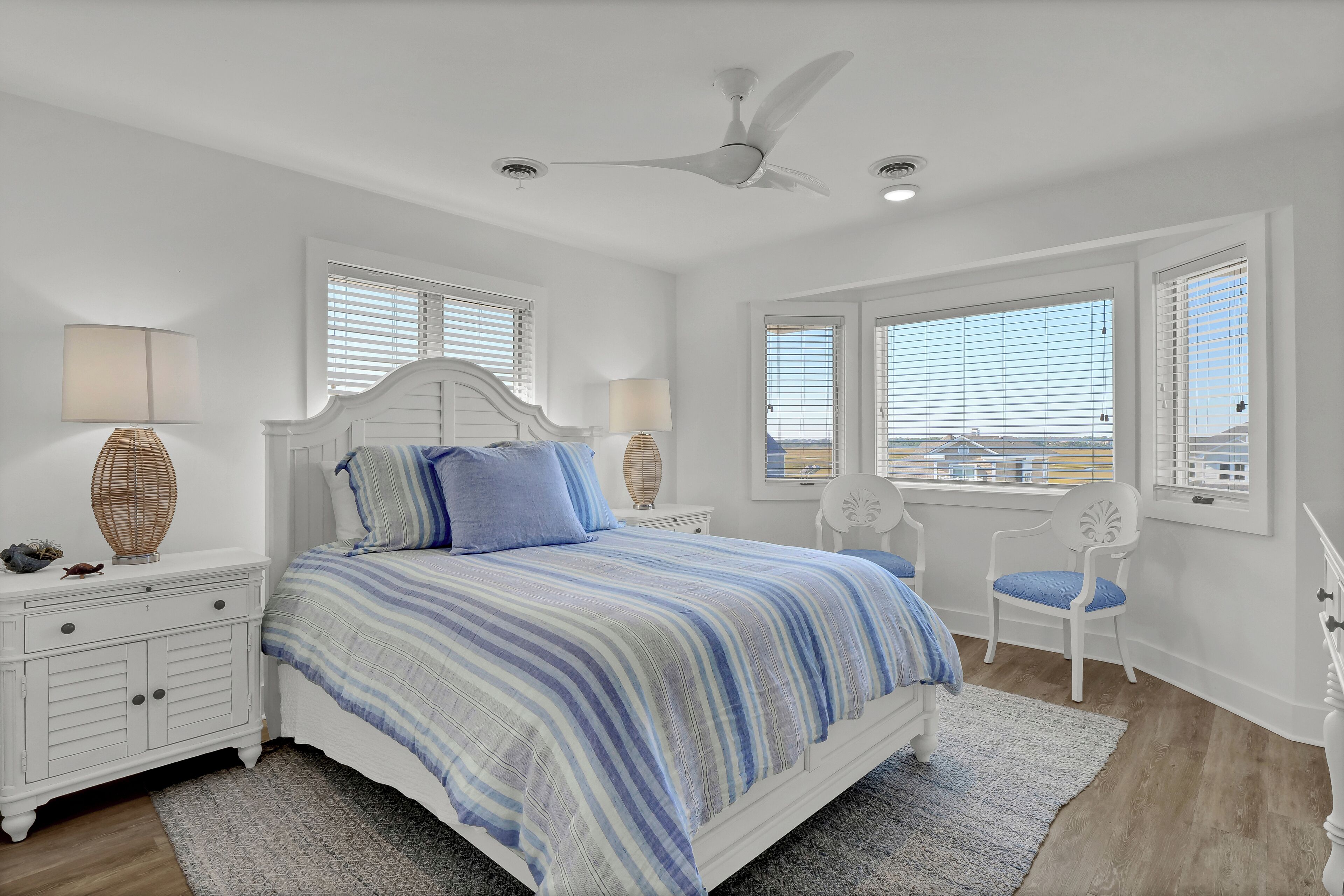 A bedroom with a bed, two nightstands, a chair, and a ceiling fan.