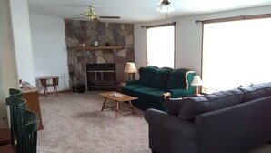 A living room with a stone fireplace, a green sofa, a grey sofa, a wooden coffee table, and a ceiling fan. - Beautiful 2-bedroom house with AC in charming Germfask  Close to Pictured Rocks (Germfask)