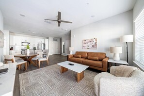A modern living room with a brown sofa, a coffee table, and a dining area with chairs and a table. - Landing | Spectacular 2BD, Gym, Pool (Palm Bay)