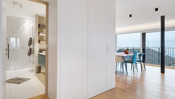 Ein modernes Interieur mit einer Glasdusche, einem Essbereich mit Tisch und Stühlen sowie einer Aussicht durch große Fenster.