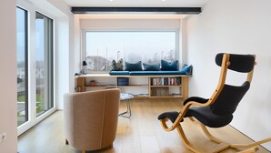 Ein modernes Wohnzimmer mit großem Fenster, einer integrierten Bücherwand, einem Schaukelstuhl und einem Sofa.