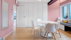 Ein modernes Interieur mit einem runden Esstisch, weißen Stühlen, einer Bank mit Kissen und einem großen Fenster.