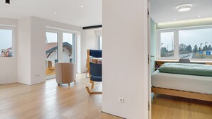 Ein modernes Schlafzimmer mit Bett, Sessel und Blick ins Freie.