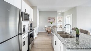 A modern kitchen with stainless steel appliances, a granite countertop, and a dining area with a table and chairs. - Landing | Chic 2BD, Pool, Gym (Palm Bay)