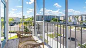 A balcony with wicker chairs, a view of a parking lot, and multi-story buildings in the background. - Landing | Chic 2BD, Pool, Gym (Palm Bay)
