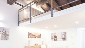 Ein geräumiger Loft mit hohen Decken, freiliegenden Holzbalken, einer Essecke mit Tisch und Stühlen sowie einer Couch.