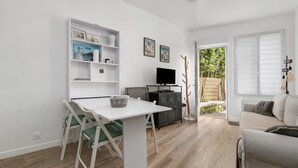 Una sala de estar moderna con una mesa de comedor blanca, sillas con acolchado verde, un sofá, un televisor y una estantería.