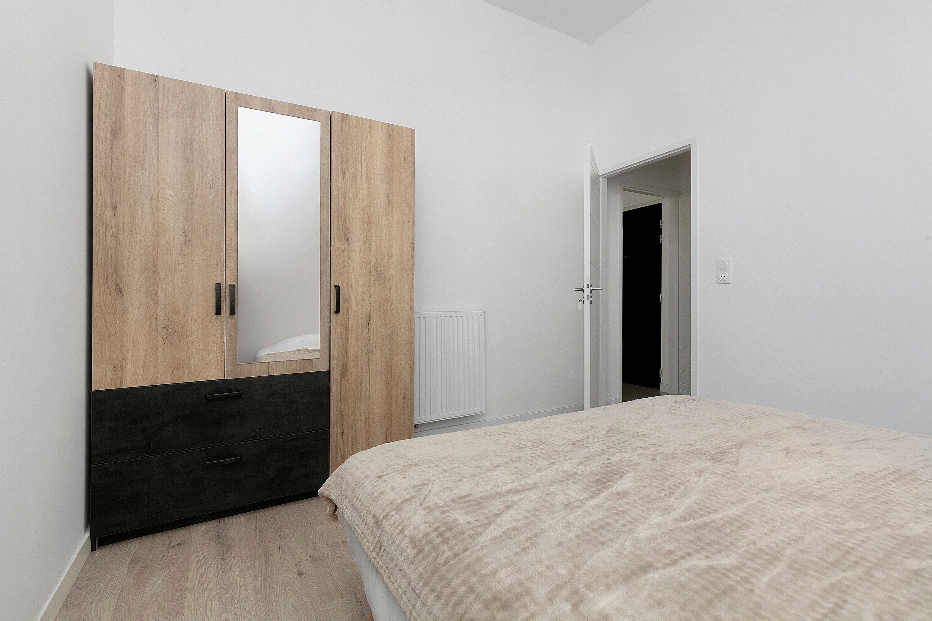 Un dormitorio con cama, armario, radiador y una puerta abierta que da a otra habitación.
