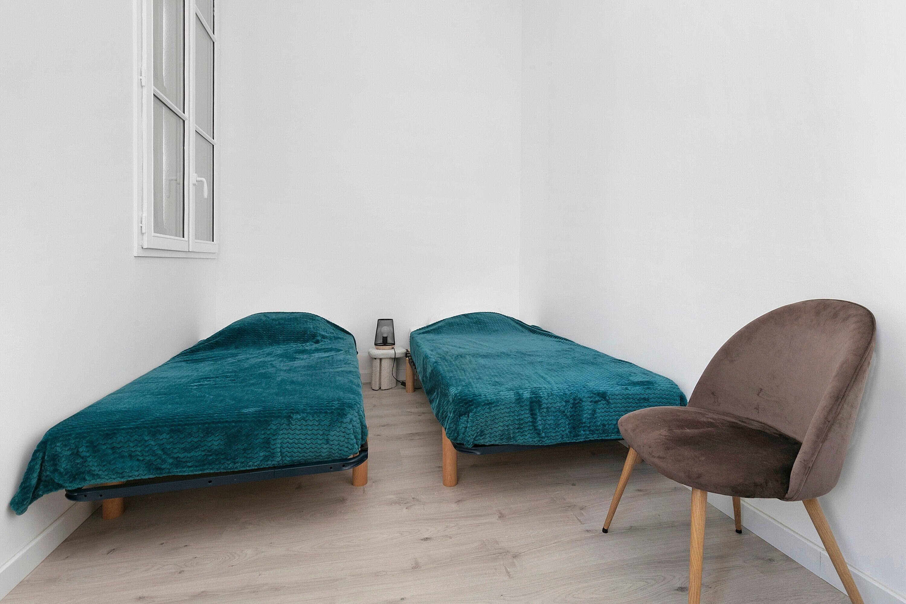 A small room with two single beds, a chair, and a small table.