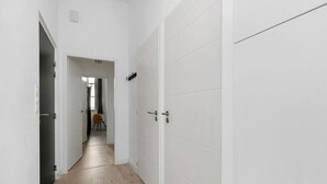Ein Flur mit weißen Wänden und Holzboden, der zu einem Raum mit Tür und Stuhl führt.