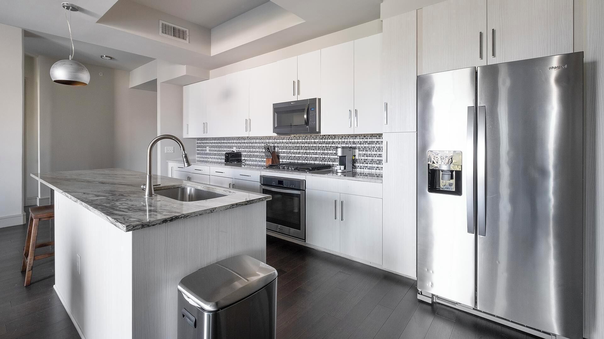 A modern kitchen with white cabinets, stainless steel appliances, a marble countertop, and a built-in microwave.