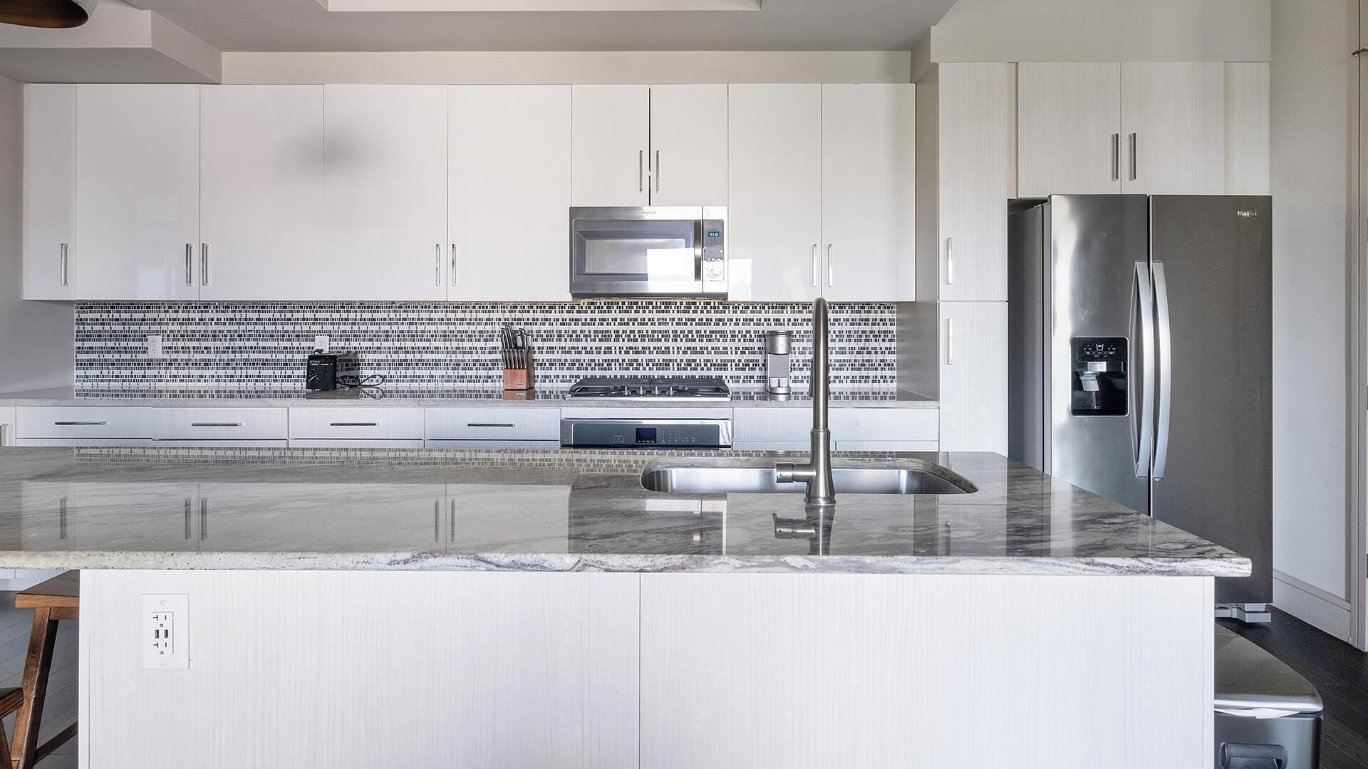 A modern kitchen with white cabinetry, a stainless steel refrigerator, and a tiled backsplash.