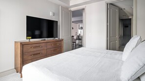 Un dormitorio con cama, cómoda, televisor y puerta que da a un baño.
