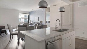 A modern kitchen with a central island, stainless steel appliances, and pendant lighting. - Landing | Amazing 2BD, Pool, Gym (Houston)