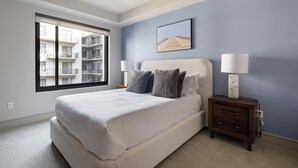 A bedroom with a large bed, two bedside tables with lamps, a window with a view of a building, and a framed picture on the wall. - Landing | Amazing 2BD, Pool, Gym (Houston)