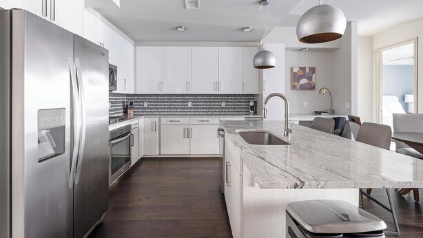 A modern kitchen with stainless steel appliances, a marble countertop, and a dining area with a view. - Landing | Amazing 2BD, Pool, Gym (Houston)