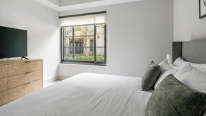 Un dormitorio con cama, cómoda, televisor y ventana con vistas al exterior.