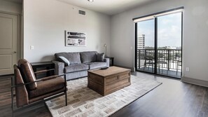 A modern living room with a grey sofa, a wooden coffee table, and a leather armchair. - Landing | Incredible 2BD, Tennis Court, Pool (Houston)