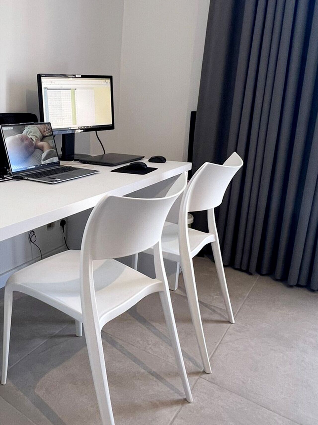 Ein moderner Büroarbeitsplatz mit weißem Schreibtisch, zwei weißen Stühlen, einem Laptop und einem Desktop-Monitor.