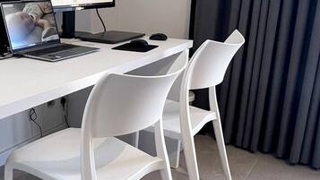 Ein moderner Büroarbeitsplatz mit weißem Schreibtisch, zwei weißen Stühlen, einem Laptop und einem Desktop-Monitor.
