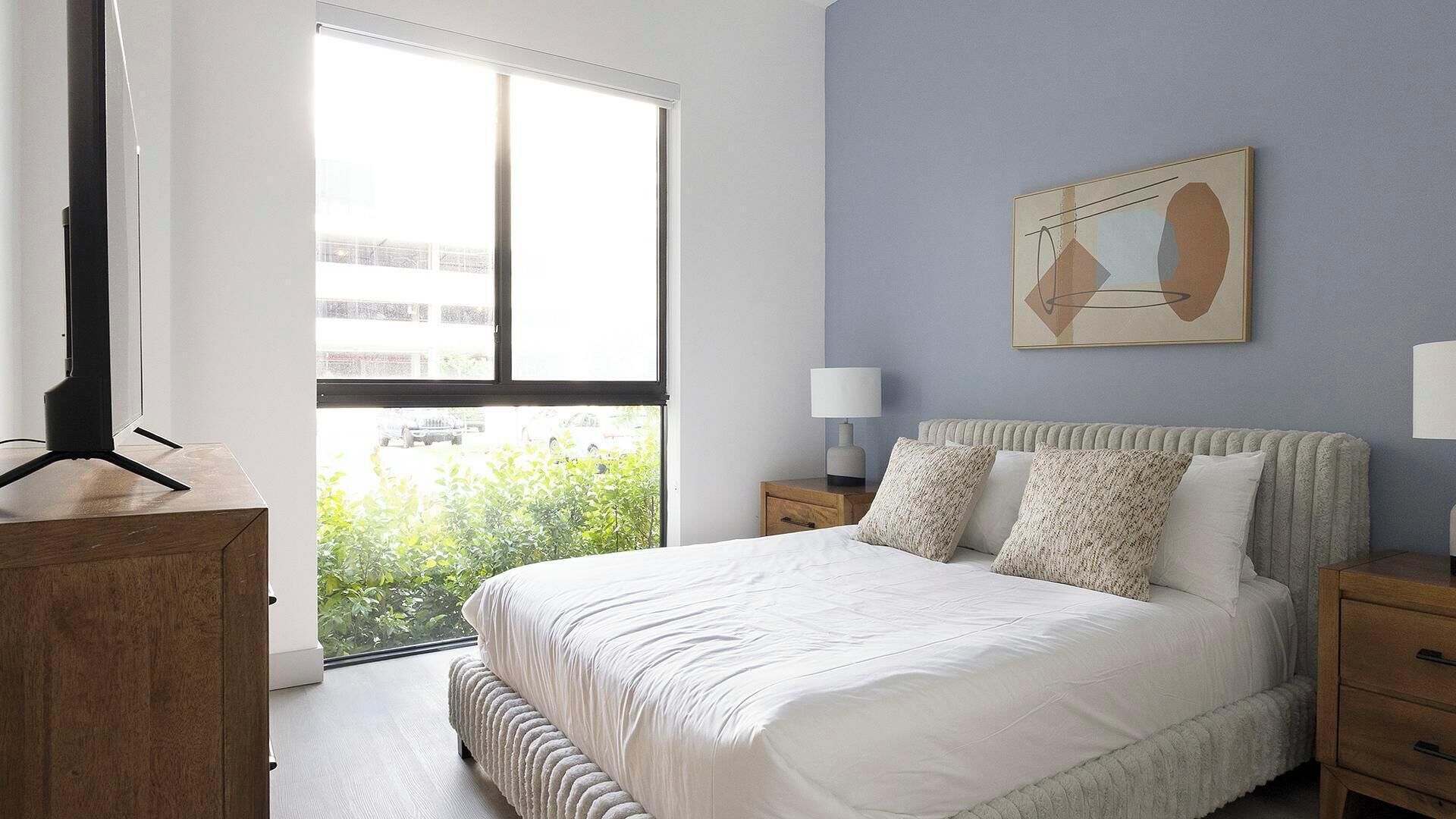Ein Schlafzimmer mit Bett, Nachttischen, einem Fenster und einem Gemälde an der Wand.